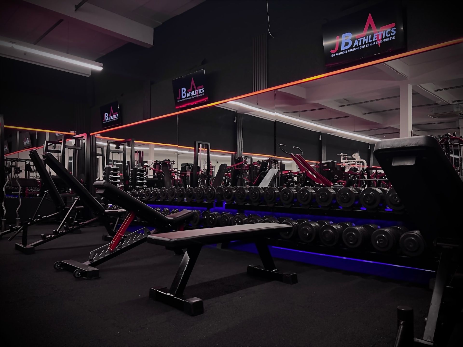 Innenansicht des Fitnessstudios der JB Athletics GmbH | Freihantelbereich mit verschiedenen Gewichten, Hantelbänken und Spiegelfront